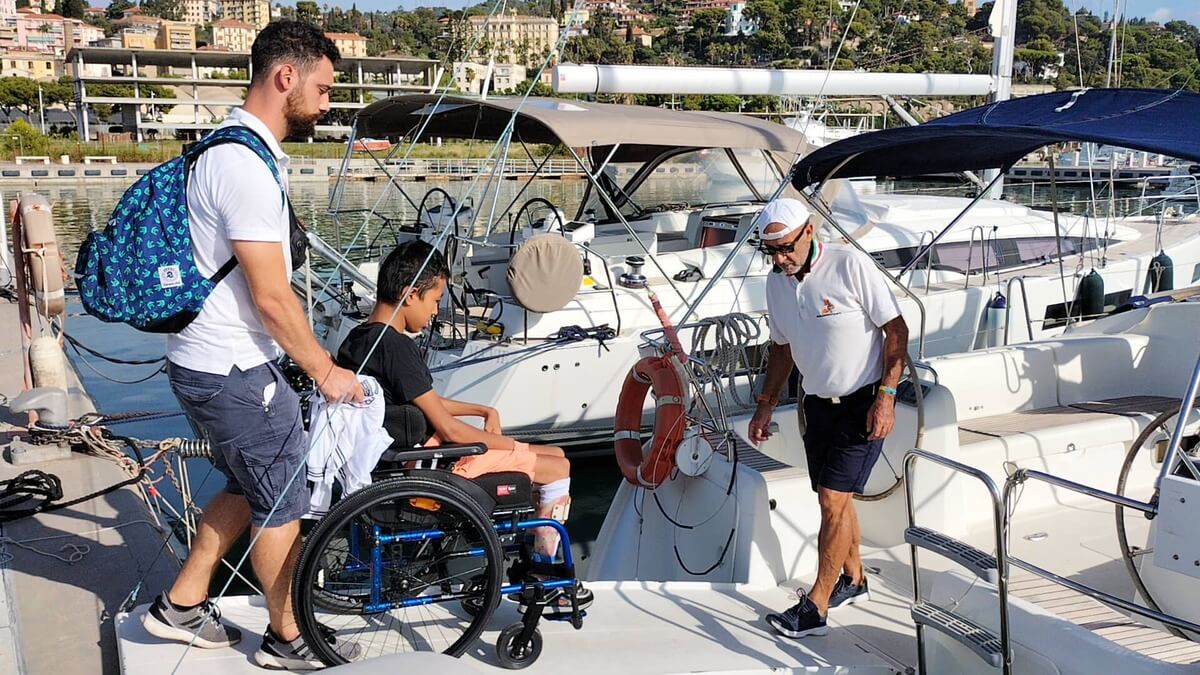 Disabile in sedia a rotelle che viene accompagnato su una barca accessibile con il supporto dei volontari Handarpermare