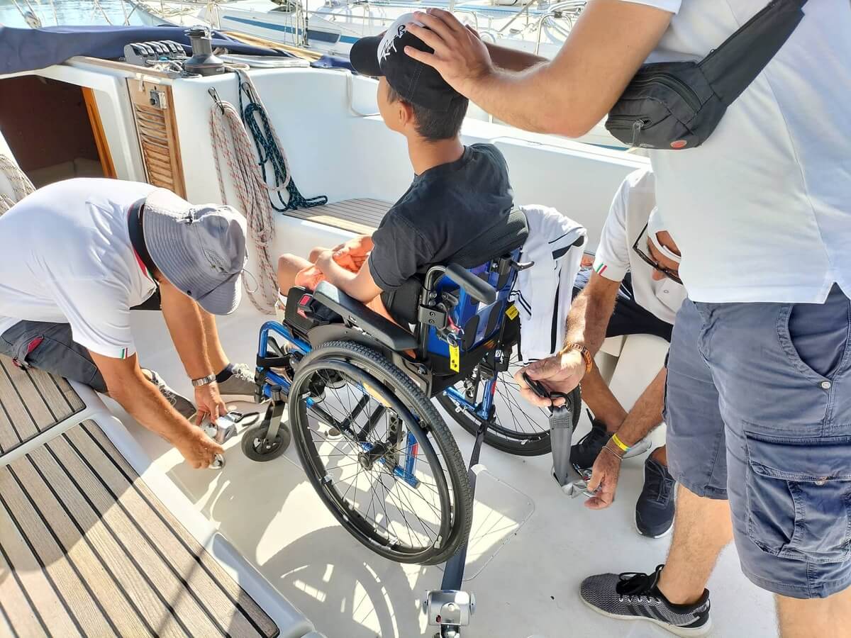 Disabile in sedia a rotelle che viene accompagnato su una barca accessibile